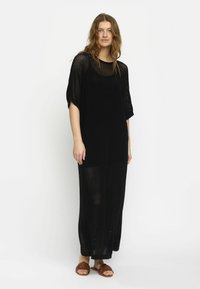 Lässig geschnittenes, schwarzes, gestricktes Maxikleid mit kurzen �Ärmeln, das über einen Rundhalsausschnitt und ein strukturiertes Muster verfügt. Getragen mit braunen Sandalen.
