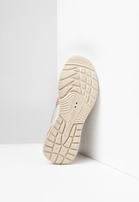 Suola di sneaker con una base in gomma testurizzata, colore beige chiaro con un accento rosa e logo in rilievo. Progettata per trazione e durata.