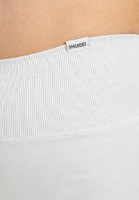 Witte geribde tailleband met een label "SMILODOX," met een gladde stoftextuur en een aansluitend ontwerp.