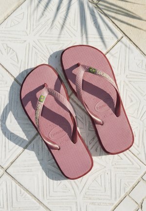 Coppia di infradito Havaianas rosa su pavimento piastrellato bianco con ombre di foglie di palma sopra.