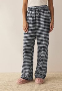 Námornícke a biele kárované pyžamové nohavice s elastickým pásom a šnúrkou, v kombinácii s ružovými plyšovými papučami na textúrovanom povrchu.