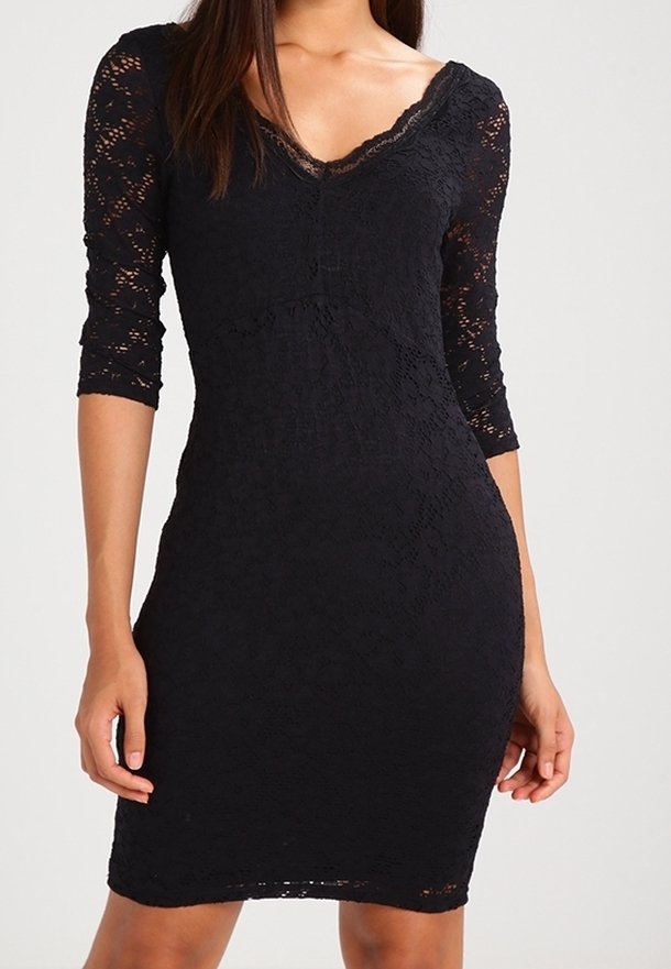 Frau in einem figurbetonten schwarzen Spitzenkleid mit Dreiviertelärmeln und V-Ausschnitt, die vor einem schlichten Hintergrund steht.