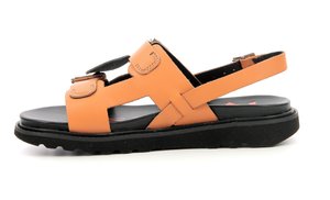 Orange leather sandal with adjustable strap, featuring a solid black rubber sole and a textured footbed. Minimalist design with cut-out details.