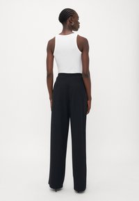 Schwarze hochtaillierte Hose mit weitem Bein, kombiniert mit einem enganliegenden weißen ärmellosen Oberteil. Glatte Stoffoberfläche mit einem subtilen Glanz.