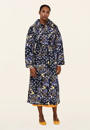 Cappotto trapuntato a fiori in navy con accenti gialli e bianchi, caratterizzato da un ampio colletto, vita stretta e una silhouette lunga e fluida.