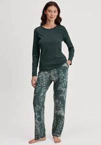 Groene lange mouw top gecombineerd met gestreepte broek met witte botanische ontwerpen op een donkergroene achtergrond. Zachte, casual stof.