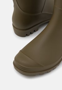Botas de chuva de borracha castanhas com bico redondo, sola texturizada e acabamento liso. Apresentam uma ligeira curvatura no tornozelo e detalhes estriados.