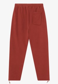 Punased dressipüksid, millel on lipsukeeps ja elastsed mansetid ning üks tagatasku. Pehme materjal sileda tekstuuriga.