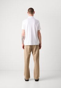 Witte polo met korte mouwen en een kraag, gecombineerd met beige broeken. Het shirt heeft een gladde textuur en een strak ontwerp.