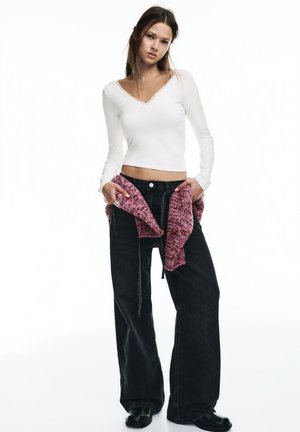 Fehér, hosszú ujjú felső csipke szegéllyel, fekete, magasderekú, bőszárú farmer, és egy texturált, rózsaszín kötött pulóver, amelyet a derékra kötve viselnek. Fekete cipő.