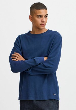 Langärmliges navyblaues T-Shirt aus weicher Baumwolle mit Rundhalsausschnitt und subtiler Logo-Akzentuierung. Texturierte Oberfläche und lockere Passform.