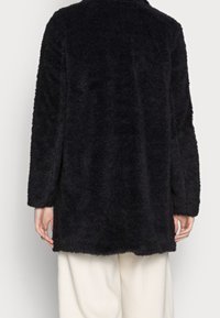 Schwarzer, flauschiger Mantel mit lockerem, schlichtem Schnitt. Verfügt über lange Ärmel und eine weiche Textur, die unter die Hüften reicht.
