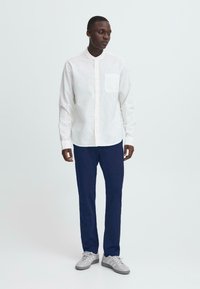 Balta garām piedurknēm pogājamā krekla ar krūšu kabatu. Apvienots ar tumši ziliem biksēm un pelēkiem kedām. Gluda auduma, kārtīga apkakle.