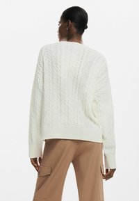 Maglione bianco a maglia con un taglio morbido, polsini e orlo a costine. Il tessuto presenta un motivo testurizzato, abbinato a pantaloni cargo beige.