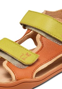 Sanda negra de cuero con dos correas ajustables verdes, una plantilla de color marrón texturizada y un gráfico de un gato en la correa. Diseño abierto para ventilación.