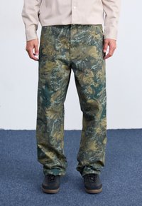 Pantaloni cargo con motivo mimetico in verde e khaki, caratterizzati da una vestibilità ampia, tessuto resistente e tasche laterali per la praticità. Abbinati a sneakers nere.