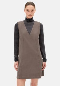 Braunes Cordkleid mit tiefem V-Ausschnitt, getragen über einem schwarz-grau gestreiften Rollkragenpullover. Glatte Textur, ärmelloses Design.