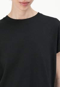 Svart kortärmad T-shirt med rund halsringning, tillverkad av mjukt, slätt tyg, med en avslappnad passform och minimala sömdetaljer.