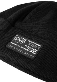 Black knitted beanie with a close-fitting design. Features a rectangular black label with white text detailing coordinates and brand name.