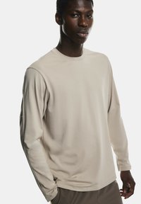 Cămașă bej cu mânecă lungă, confecționată dintr-un material moale, având guler rotund și croi drept. Textură netedă, fără modele sau accente vizibile.