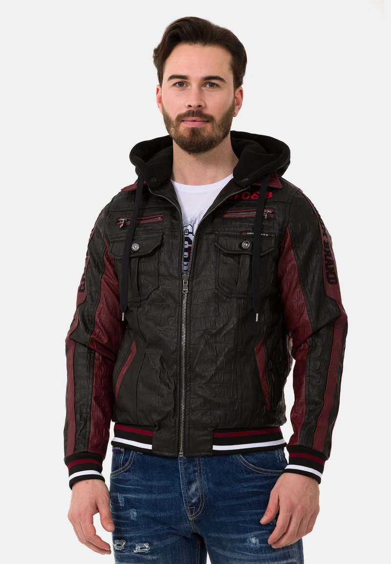 Lederjacke mit einer strukturierten schwarzen Oberfläche, burgunderfarbenen Akzenten, einem Reißverschluss vorne und einer Kapuze. Enthält mehrere gefütterte Taschen mit Reißverschluss und gestreifte Bündchen.