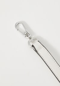 Hvitt lærrem med svart kant, med en sølvmetallklips og ring for feste. Overflaten er glatt med synlig søm.