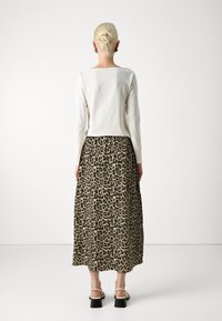 Un haut blanc à manches longues associé à une jupe midi à imprimé léopard. La jupe présente une texture fluide et une légère forme A, avec des accents noirs.