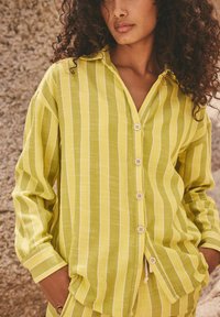 Camicia a righe verde chiaro con una chiusura a bottoni davanti, colletto e maniche lunghe, dal taglio relax. Il tessuto presenta una finitura texturizzata.