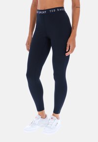 Granatowe legginsy treningowe o dopasowanym kroju, z kontrastującą czarną gumą w pasie i białym logo. Gładki, elastyczny materiał z subtelnymi szwami.