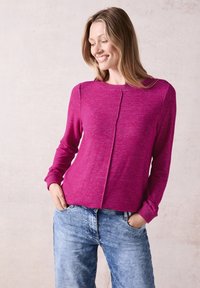 Pull en tricot fuchsia à manches longues, avec un détail de couture sur le devant. Associé à un jean en denim bleu clair et décontracté. Texture lisse.