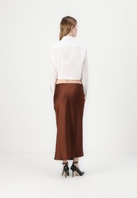 Hvitstripete cropped skjorte, brun sateng midi skjørt, svarte høyhælte sko, glatt tekstur, tettsittende design, sett fra baksiden.