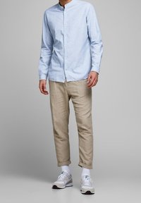 Ljusblå skjorta med mandarin-krage, kombinerad med beige linnebyxor och vita sneakers. Slätt tyg, avslappnad passform.