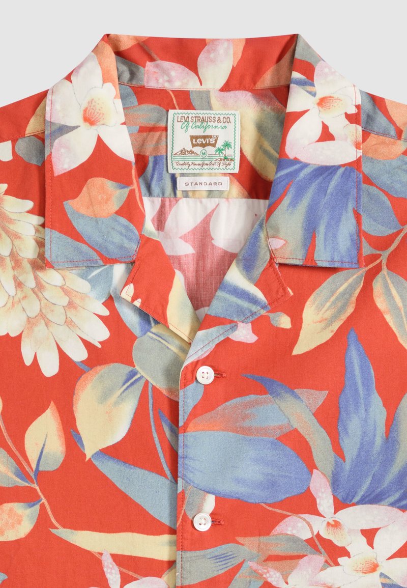 Camisa roja de manga corta con botones y gran estampado floral en blanco, azul y beige, con una etiqueta Levi's dentro del cuello.