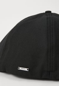 Black cap with a structured design, made of smooth fabric. Features a small silver logo tag on the side and a rounded crown.