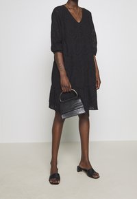 Černé šaty s průstřihy a v-výstřihem a tříčtvrtečními rukávy, doplněné malou černou kabelkou s krokodýlím embosováním a černými skládacími sandály.