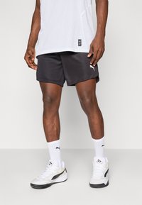 Svarte atletiske shorts med løs passform, kombinert med hvite sokker og svart-hvite sneakers. Toppdelen har et strukturert mesh-design.