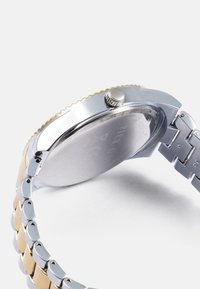 Stainless steel and gold-tone wristwatch with a round case, textured bezel, and linked band featuring alternating silver and gold links.