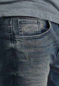 Tamno plavi traperice s stražnjim džepom s iznošenim rubovima i suptilnim istaknutim kamenim pranje, uparene sa sivosmešavom majicom.