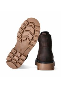 Stivaletto in pelle marrone con suola in gomma robusta. La suola presenta una profonda scolpitura per una migliore aderenza ed è costruita per resistere all'usura. Il retro mostra un manico per facilitare l'inserimento.