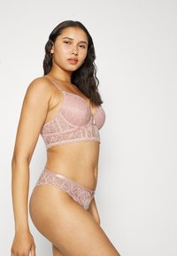 Conjunto de lingerie em renda na cor rosa suave, apresentando um sutiã acolchoado com padrão floral e borda scalloped, emparelhado com cuecas de renda coordenadas.