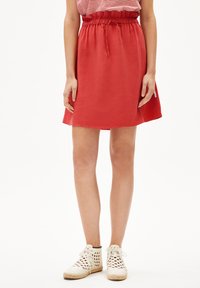 Falda roja hasta las rodillas con una cintura elástica ajustable. Textura suave y un ligero vuelo en el dobladillo. Combinada con zapatos blancos de tejido.
