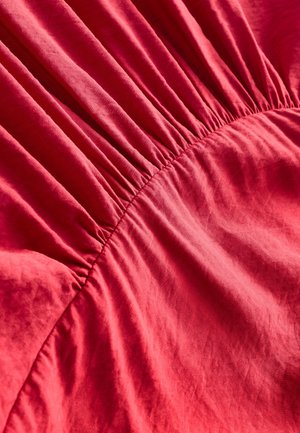 Material roșu cu textură adunată în centru, evidențiind un material moale, neted și un luciu subtil.