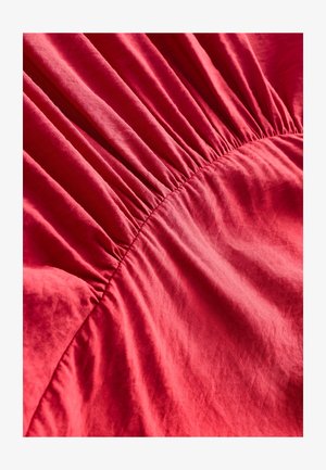 Piros szövet, amely a közepén gyűrt textúrával rendelkezik, lágy, sima anyagot és finom fényű felületet mutatva.