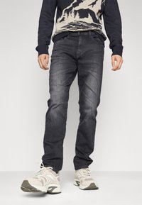 Jeans de color gris oscuro con un ajuste slim, combinados con un suéter de punto azul marino y zapatillas deportivas neutrales. Presentan costuras visibles y un diseño de cinco bolsillos.
