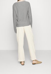 Grijze geribbelde trui, crèmekleurige wijde broek en geweven beige instappers. Ontspannen pasvorm en omgeslagen mouwen van de broek, eenvoudig ontwerp.