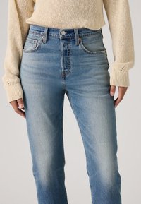 Φωτεινό γαλάζιο τζιν με ψηλή μέση, στενή γραμμή, χαλκινο εξάρτημα και διακριτική ξεθώριαση. Συνδυασμένο με κρεμ  πλεκτό πουλόβερ.