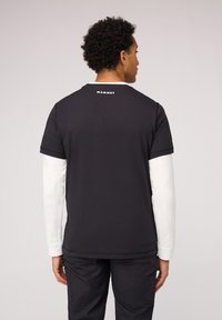 Zwarte t-shirt met korte mouwen en een wit logo op de achterkant, gelaagd over een wit shirt met lange mouwen. Casual pasvorm en gemaakt van katoen.