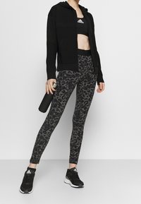 Veste à capuche noire zippée sur un soutien-gorge de sport noir, accompagnée de leggings ajustés à motif léopard gris et de chaussures de sport noires.