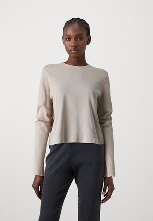 Beige långärmad topp med rund halsringning och slät textur, kombinerad med mörka randiga byxor. Enkel och figurnära design.