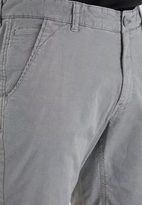 Pantalons en coton mélangé gris avec une texture lisse, dotés d'un devant plat, de poches latérales et de coutures décoratives le long des coutures.